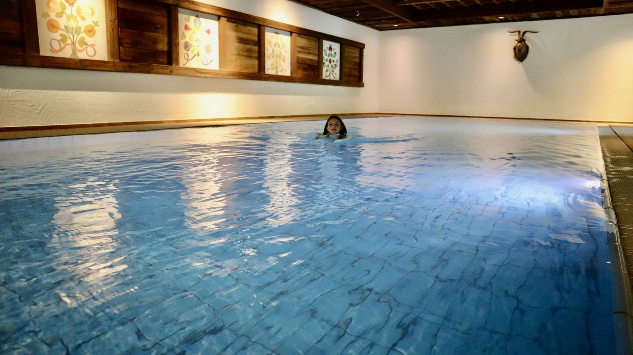Frau schwimmt in einem Innenpool mit Holzwänden und dekorativen Bildern an der Wand