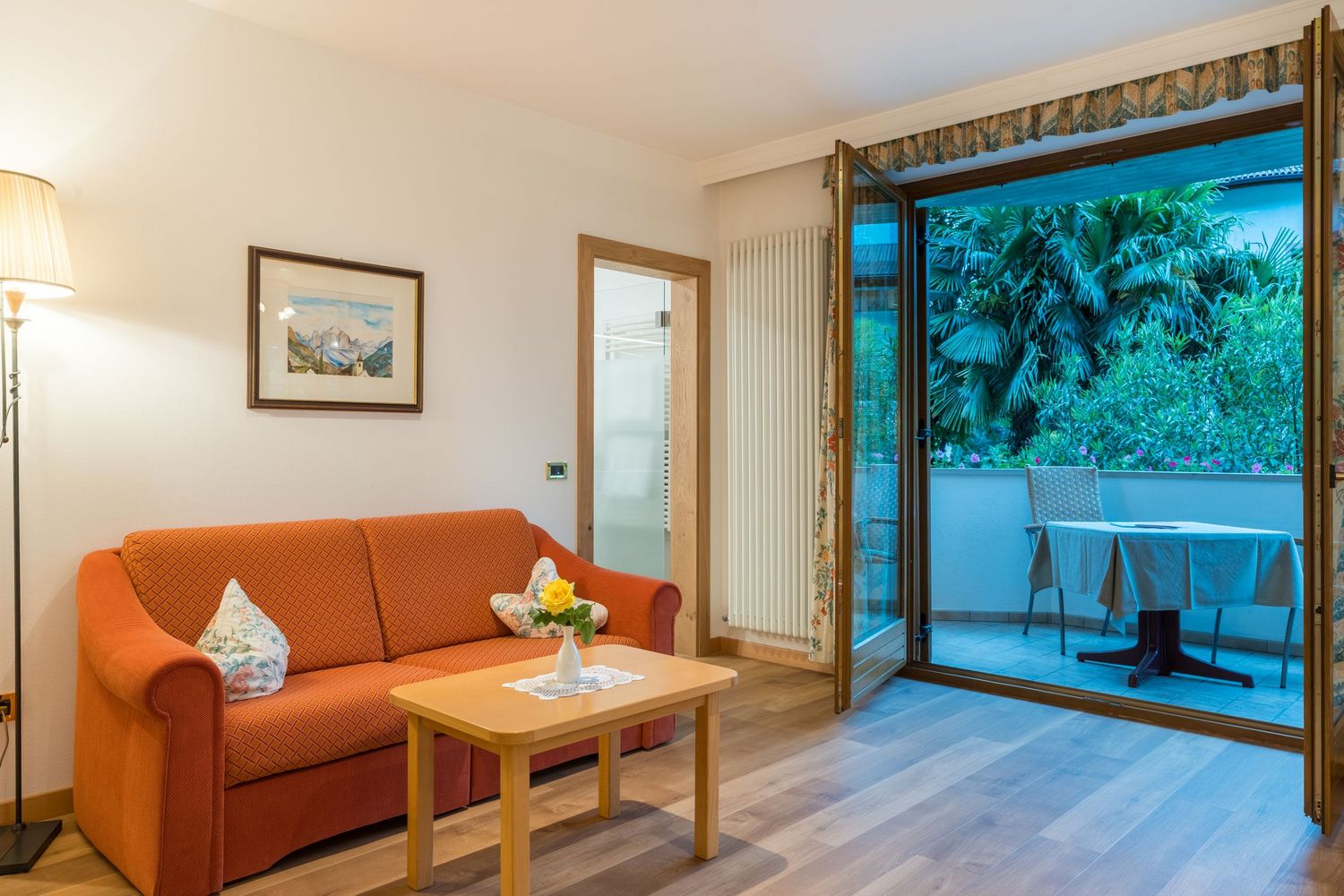 Gemütliches Wohnzimmer mit rotem Sofa, Holz-Couchtisch und offener Tür zur Terrasse mit Gartenblick.
