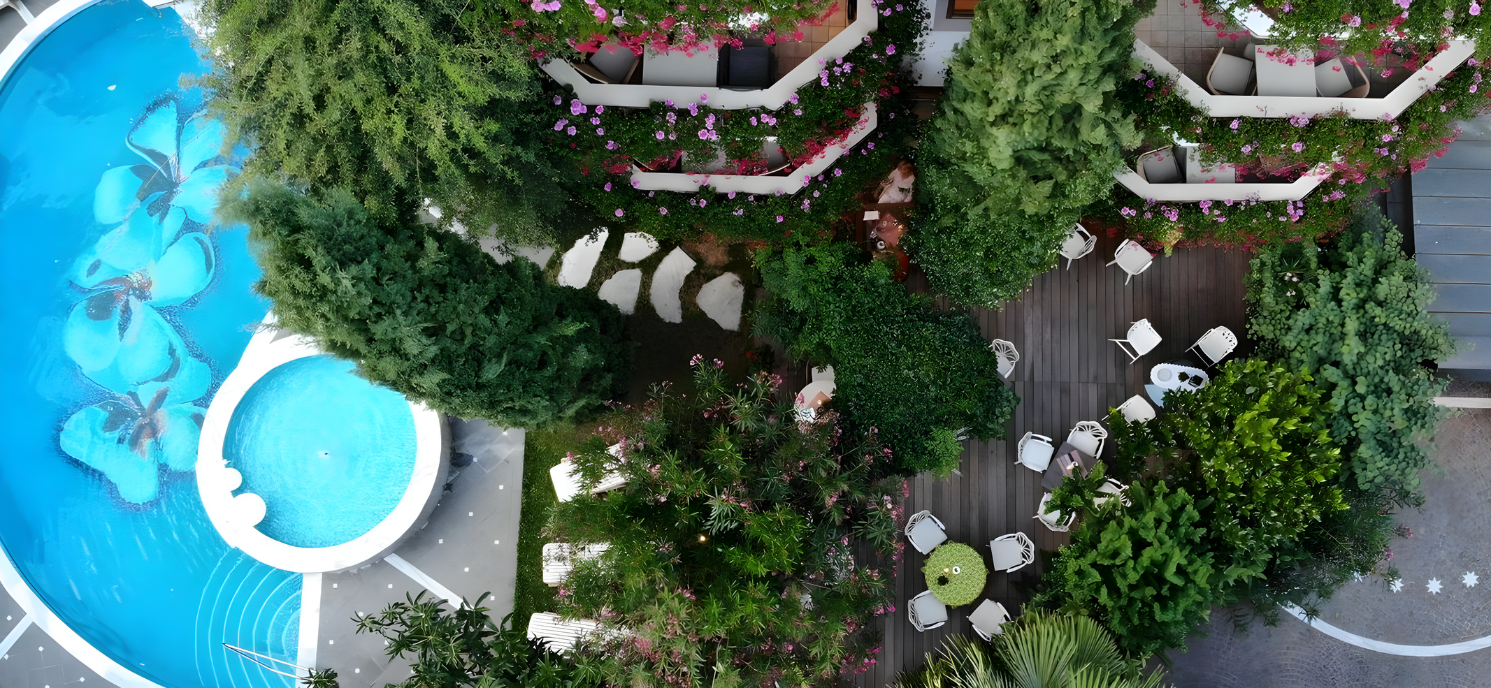 Aerial view of a courtyard with a swimming pool featuring floral designs, surrounded by greenery, outdoor seating, and flowering balconies.