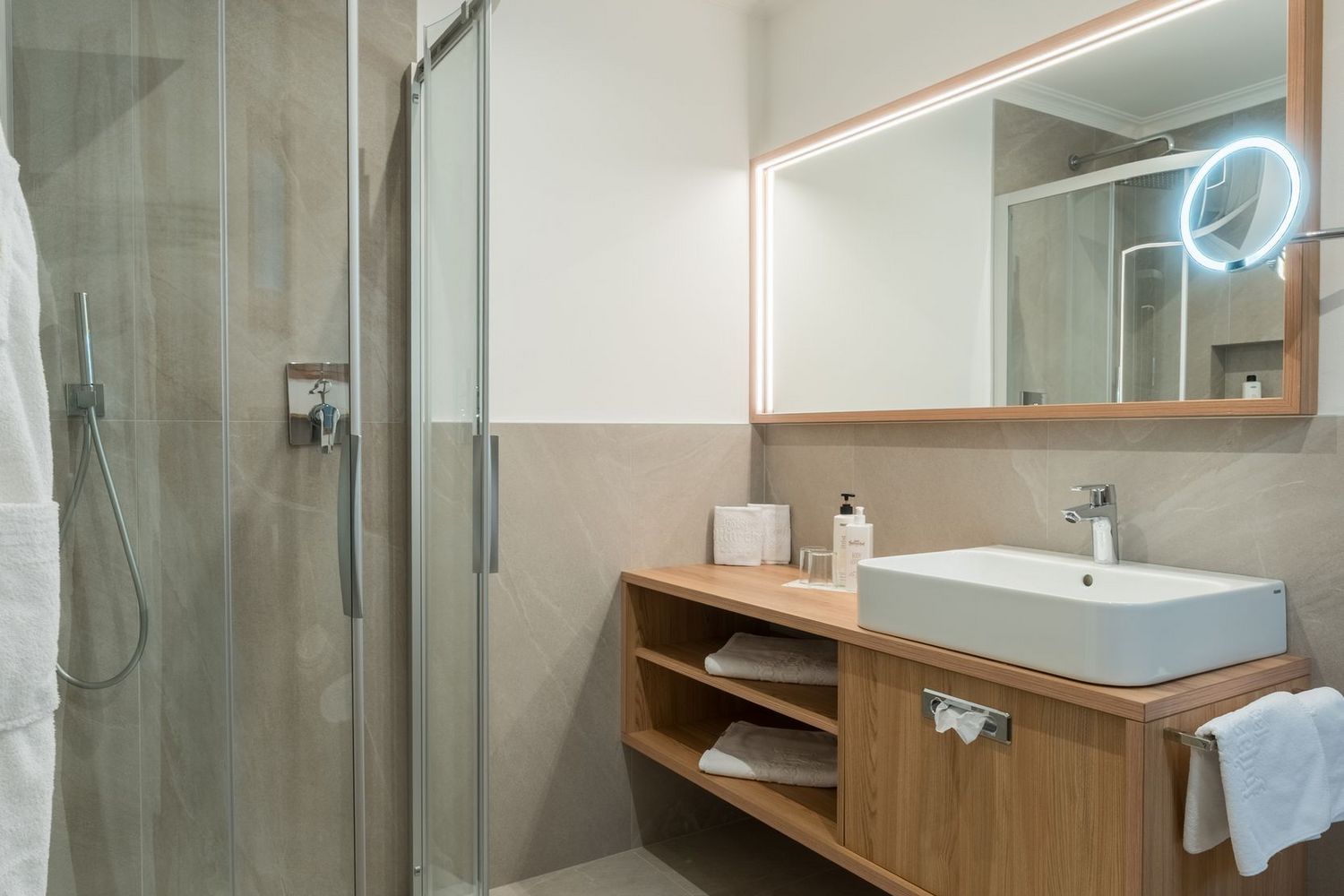 Modernes Badezimmer mit Runddusche, Waschtisch aus Holz und beleuchtetem Spiegel