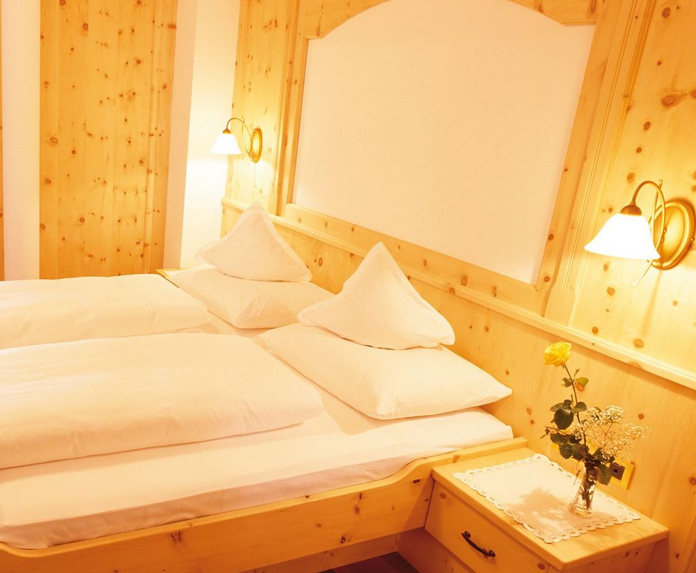 Camera da letto in legno con letto doppio, comodino con vaso di fiori e balcone con tavolo e sedie