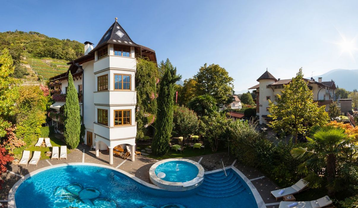 Sonniger Garten mit Pool, Liegestühlen und traditionellen Gebäuden, umgeben von grünen Bergen und Herbstbäumen.