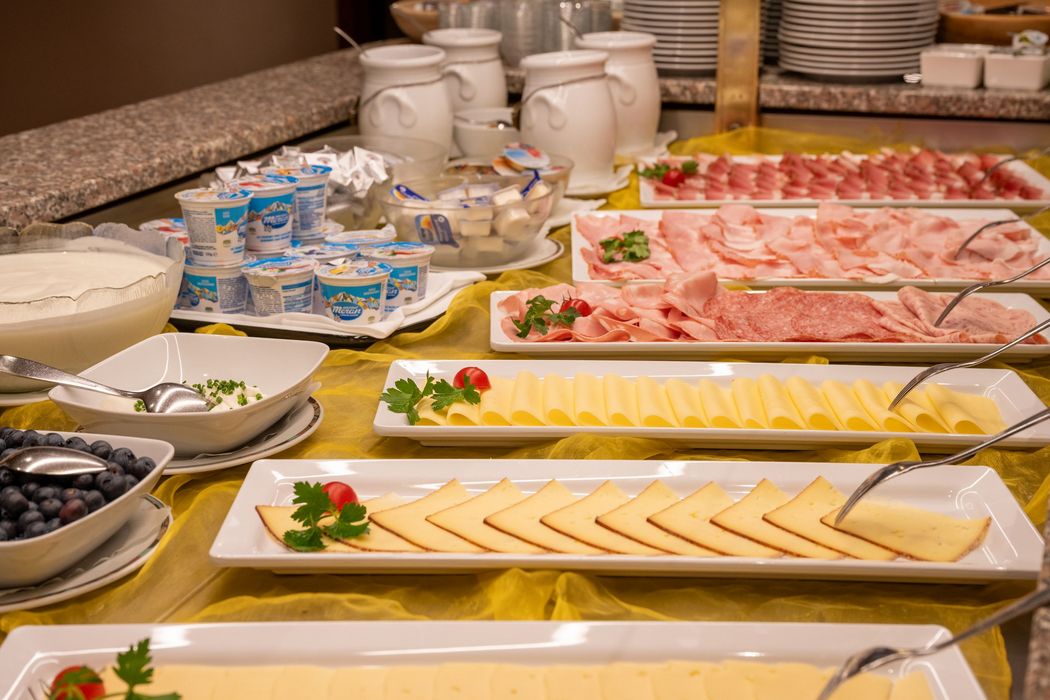 Buffet mit verschiedenen Käsesorten, Wurstplatten, Joghurts und Beeren auf weißen Tellern und Schalen.