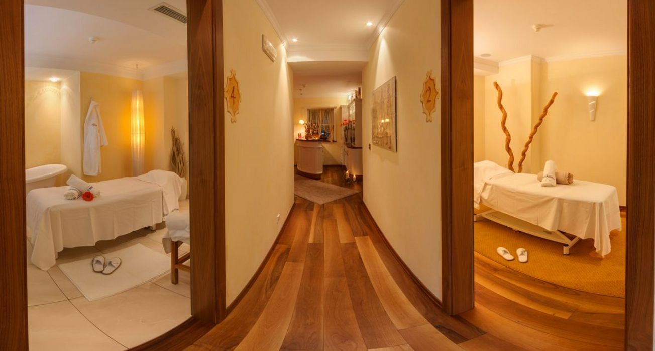 Flur mit mehreren Türen zu Behandlungsräumen in einem Wellness- oder Massagestudio mit warmem Holzfußboden und Gelbtönen.