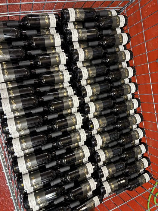 Viele Flaschen Lagrein Rotwein liegen nebeneinander in einem Einkaufswagen auf rotem Boden.