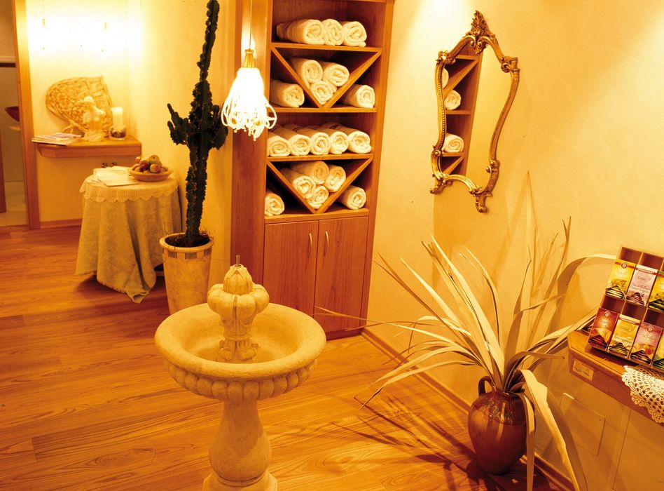 Gemütlicher Spa-Wartebereich mit Holzregal voller Handtücher, Pflanzen, Spiegel und warmem Licht.