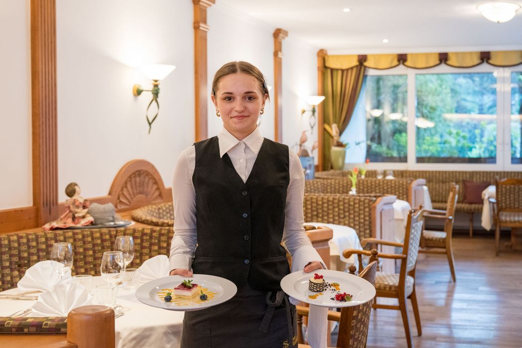 Junge Kellnerin in Restaurant trägt zwei Teller mit Desserts.