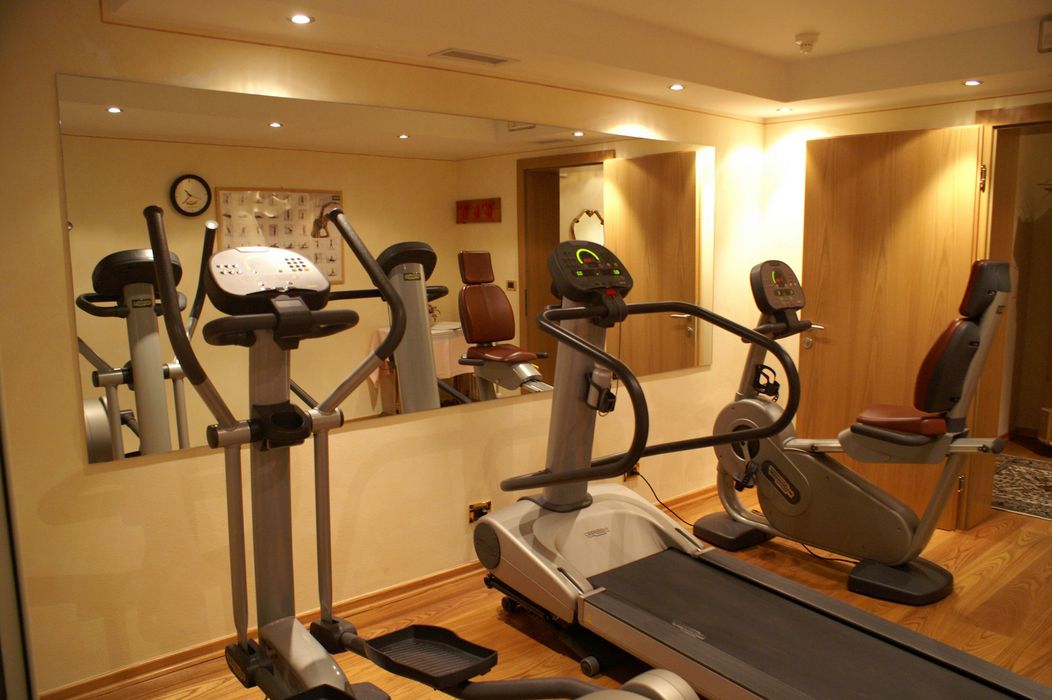 Kleiner Fitnessraum mit Crosstrainer, Laufband und Sitzfahrrad vor Wand mit großem Spiegel