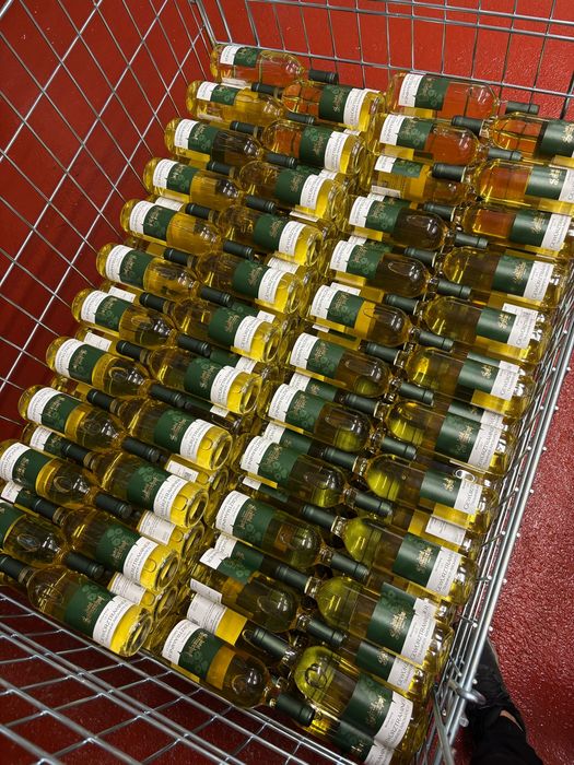 Gefüllter Einkaufswagen mit vielen Flaschen Weißwein vor rotem Hintergrund