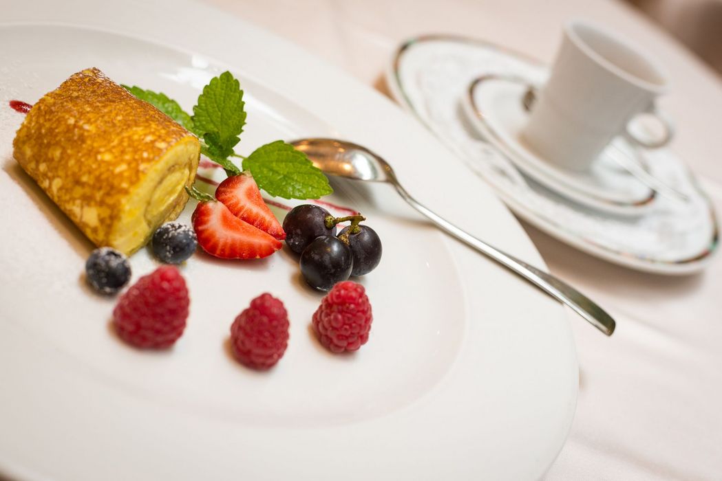 Dessertteller mit einer Rolle Pfannkuchen, frischen Beeren und Minzblatt, daneben ein Löffel und eine Tasse auf einer Untertasse