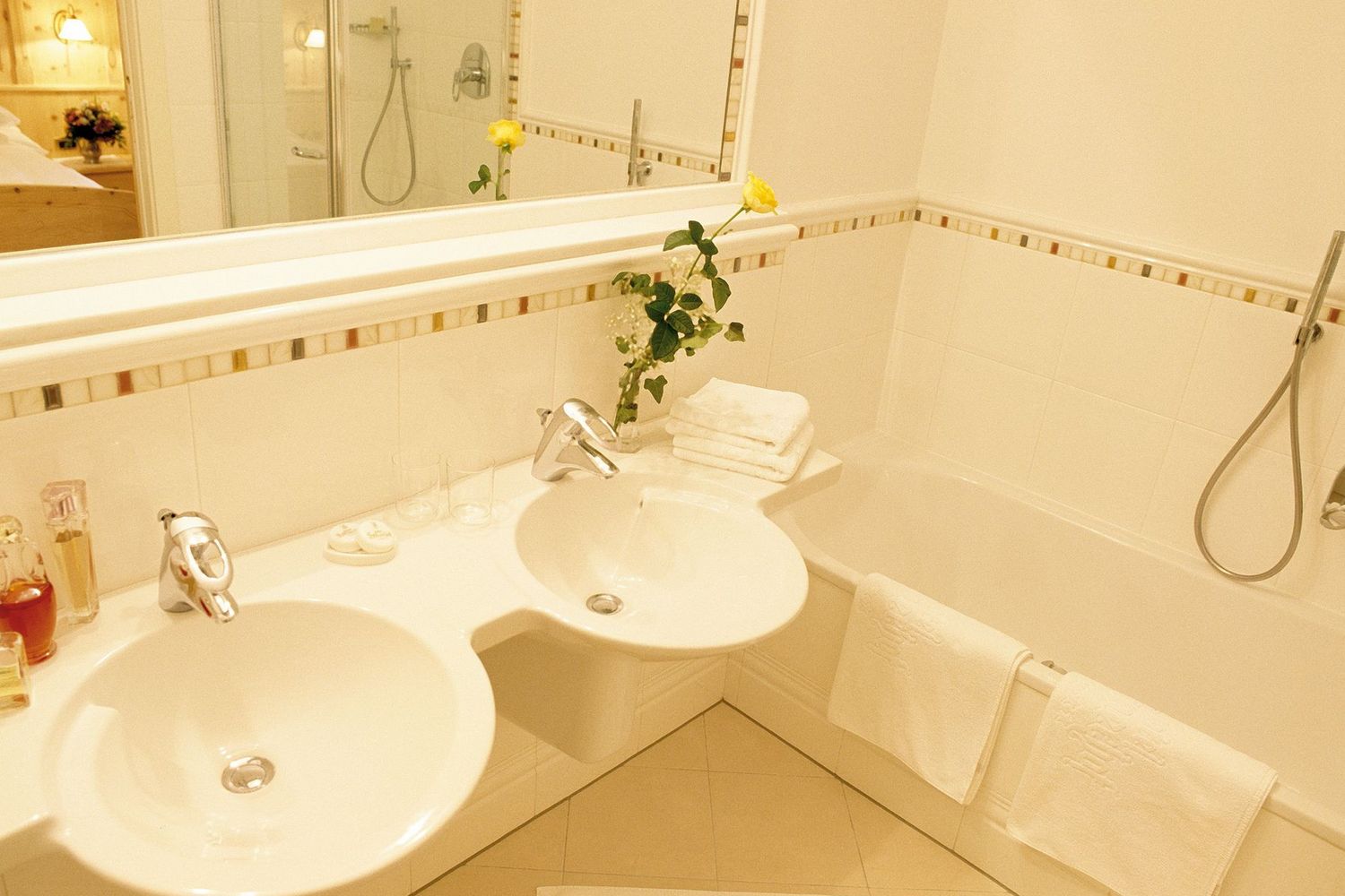 Helles Badezimmer mit zwei Waschbecken, Badewanne, Handtüchern und gelber Blume in Vase
