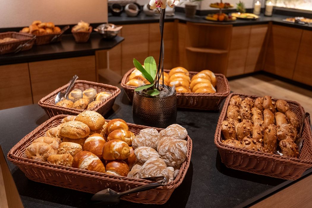 Verschiedene Brotsorten und Brötchen in Körben auf einem Buffet mit einer Blume in der Mitte