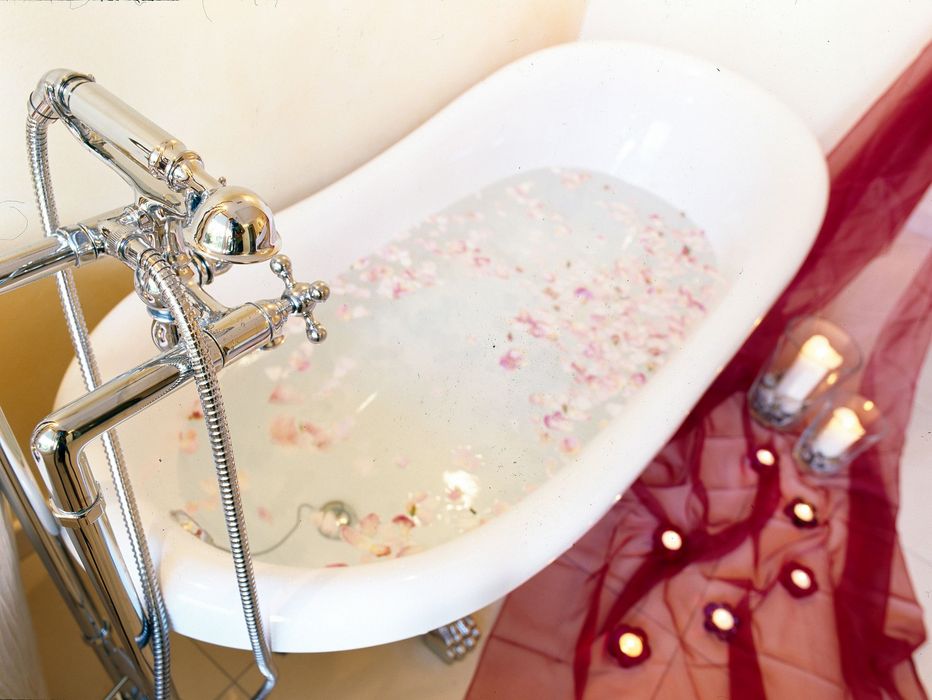 Clawfoot bathtub filled with water and flower petals, surrounded by candles and red fabric on the floor