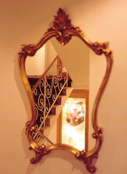Spiegel mit verziertem goldenem Rahmen, der eine Treppe und ein beleuchtetes Bild einer lächelnden Frau reflektiert
