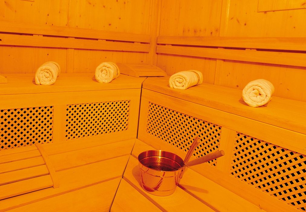 Holzsauna mit vier aufgerollten Handtüchern und einem Metallkessel auf der Bank