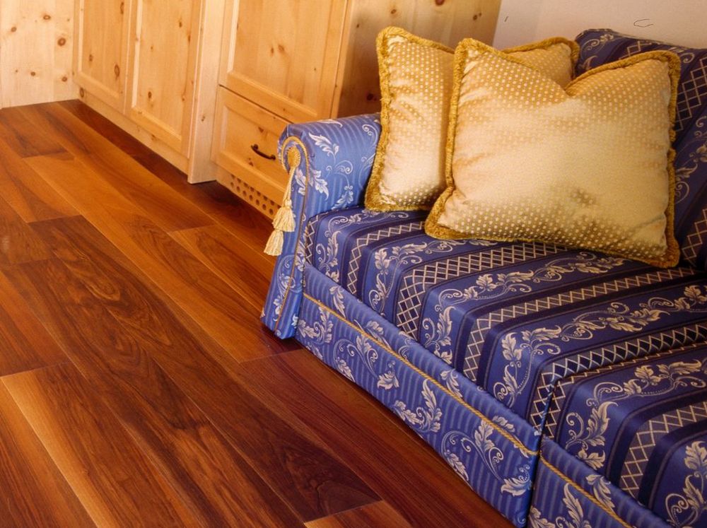 Interno accogliente con pavimento in legno, tavolo rotondo, divano blu con cuscini e mobile con laptop.