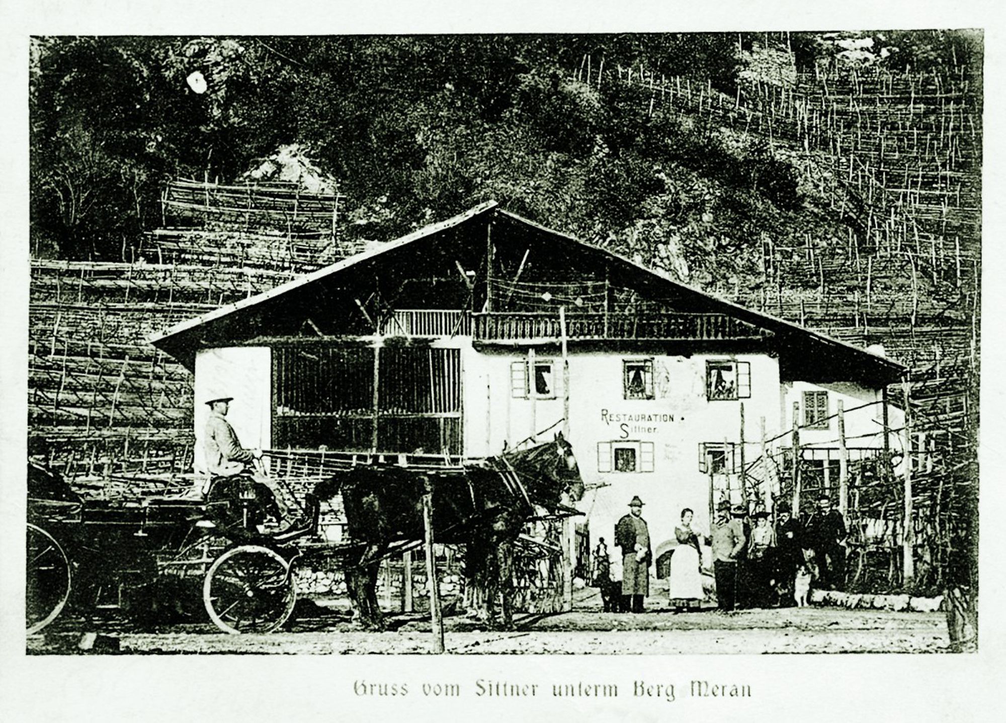 Historic black and white photo of a mountain inn with people standing outside and a horse-drawn carriage in front.